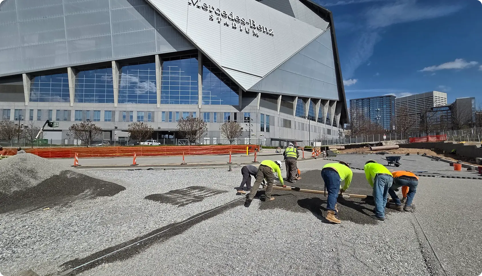Construction workers leveling gravel near stadium.